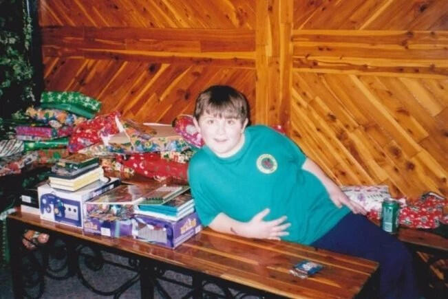 Young boy lies on a brown bench wearing green shirt.